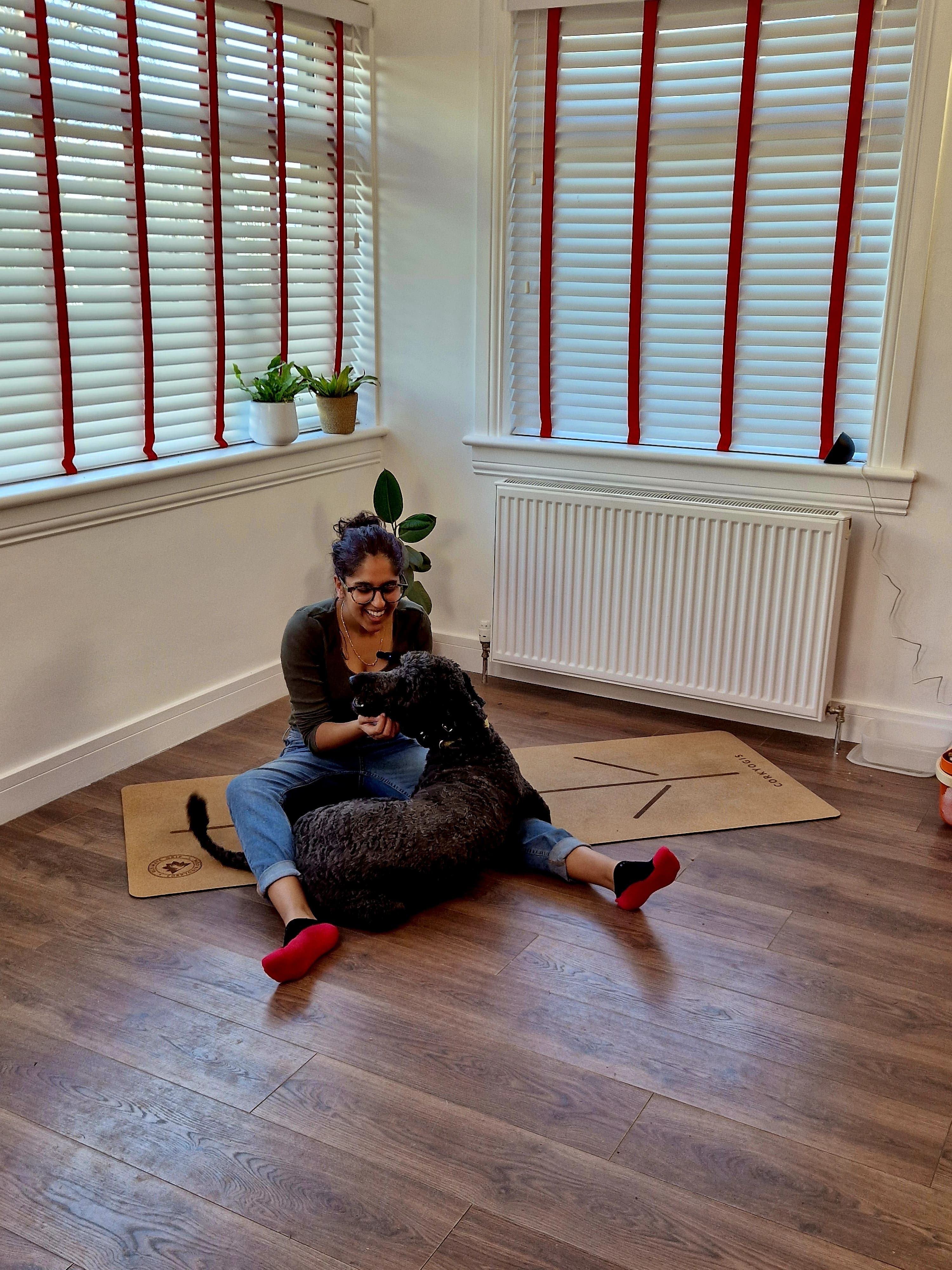 Shruti with her large fluffy black dog, Bonnie, sat on Shruti's yoga mat in her at-home studio.